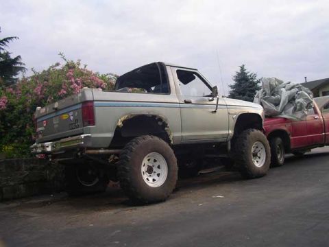1984 Ford Bronco II - This lifted pickup truck has large off-road tires and is parked next to another truck.