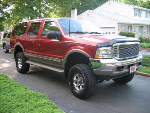 2001 Ford Excursion - A red Ford Excursion is parked on a driveway with a house and trees in the background.