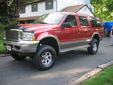 2001 Ford Excursion - A red Ford Excursion SUV is parked in front of a house, showing its side and front quarter view.