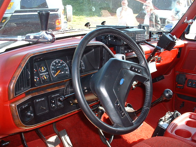 Red Ford truck interior with black steering wheel, woodgrain dash trim, and floor shifters