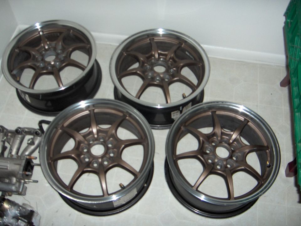 Four bronze multi-spoke alloy wheels with polished lips on a tile floor