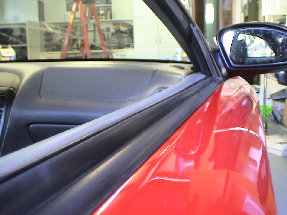 Close-up of red car door frame and interior dashboard, with a side mirror visible