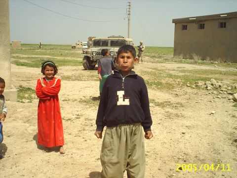 1988 Mercury Sable - Children stand in a dirt area with a military vehicle and soldier visible in the distance.