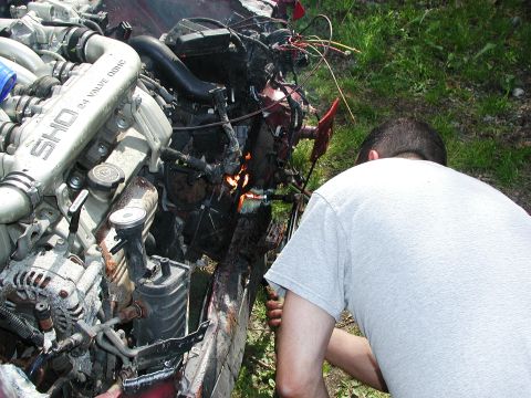 1992 Ford Taurus - A person works on the damaged engine of a 1992 Ford Taurus SHO, with visible 'SHO 3.0L 24 VALVE DOHC' badging.