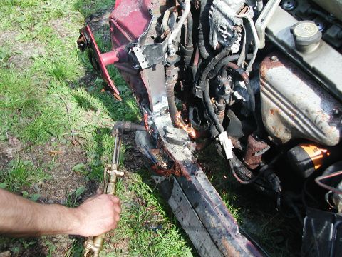 1992 Ford Taurus - A person uses a torch to cut into the damaged frame of a red car, with the engine visible.