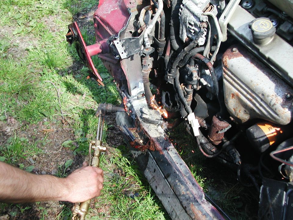 Damaged red car frame and engine being cut with a torch