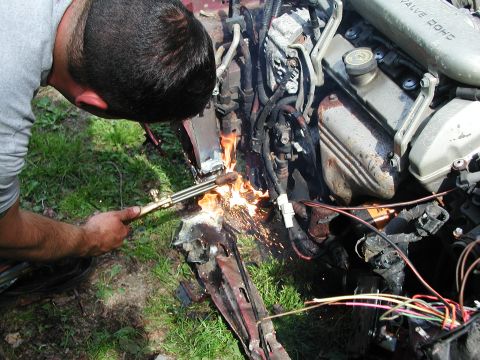 1992 Ford Taurus - A person uses a cutting torch on the engine bay of a 1992 Ford Taurus, with 'VALVE DOHC' visible on a component.