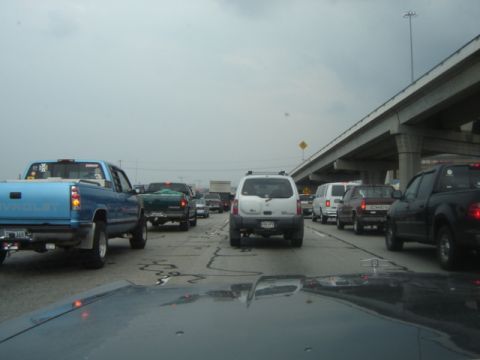 1988 Ford Crown Victoria LTD - Multiple vehicles are stopped in traffic on a highway under a concrete overpass.