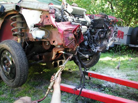 1992 Ford Taurus - A heavily damaged vehicle's front end is being cut with a torch while supported by a red engine hoist.