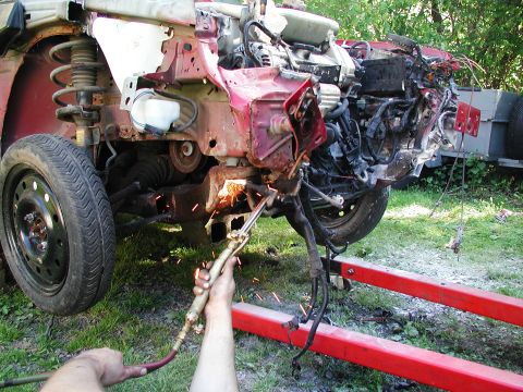 1992 Ford Taurus - A person uses a torch to cut away the front end of a red car, revealing its engine and suspension.