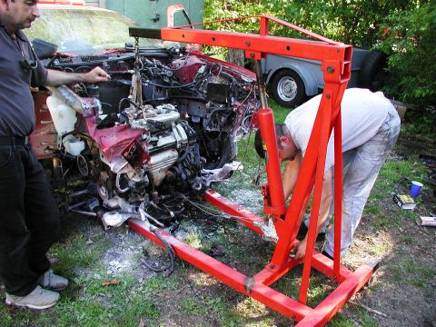 1992 Ford Taurus - Mechanics work on removing the engine from a red 1992 Ford Taurus using an engine hoist.