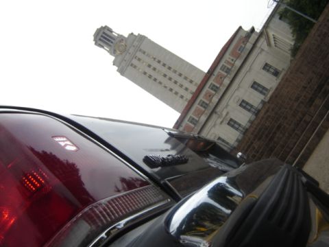 1988 Ford Crown Victoria LTD - A car's taillight and trunk are visible with a tall clock tower in the distance.