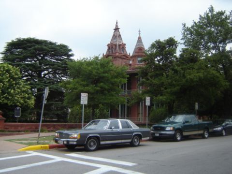 1988 Ford Crown Victoria LTD - A dark gray sedan is parked on the street next to a green pickup truck, with a historic building in the background.