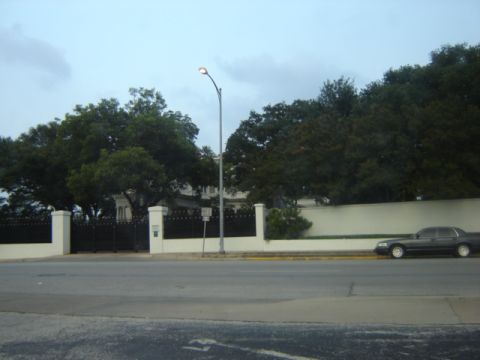 1988 Ford Crown Victoria LTD - A dark sedan is parked along a street in front of a large building with a white wall and black gates.