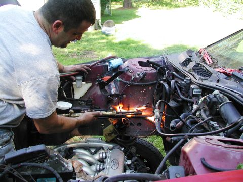 1992 Ford Taurus - A man uses a cutting torch on the engine compartment of a vehicle outdoors.