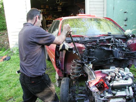 1992 Ford Taurus - A mechanic works on the front end of a disassembled 1992 Ford Taurus, revealing the engine and suspension.