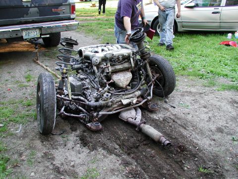 1992 Ford Taurus - The front subframe and engine assembly of a car are on the ground, with people and other vehicles in the background.