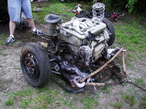 1992 Ford Taurus - This image shows a disassembled engine and front suspension assembly, including a tire, resting on the ground.
