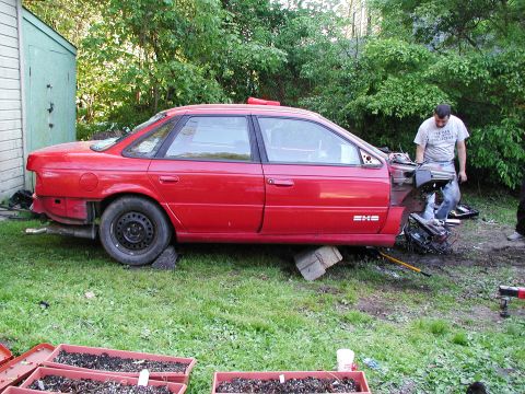 1992 Ford Taurus - A red sedan is parked in a yard with its front end removed, and a person is working on the engine components.
