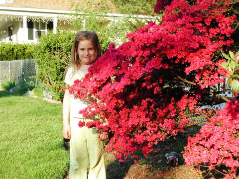 1992 Ford Taurus - A young girl poses in front of a vibrant flowering bush, with a house and yard visible behind her.