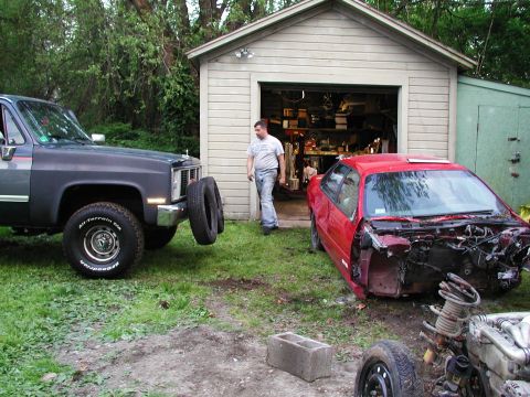 1992 Ford Taurus - Two vehicles are parked in a yard near a garage, one is a red car with its front end removed.