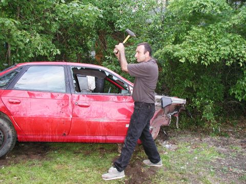 1992 Ford Taurus - A man prepares to smash a red 1992 Ford Taurus sedan with a hammer, its windows shattered.