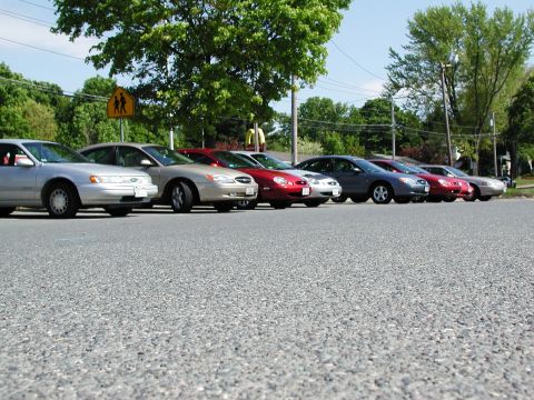 1992 Ford Taurus - A row of sedans, including a silver 1992 Ford Taurus, are parked along a street on a sunny day.