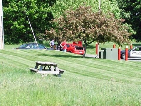 1992 Ford Taurus - A police car is partially submerged in a grassy ditch while several people stand near a red sedan with its trunk open.