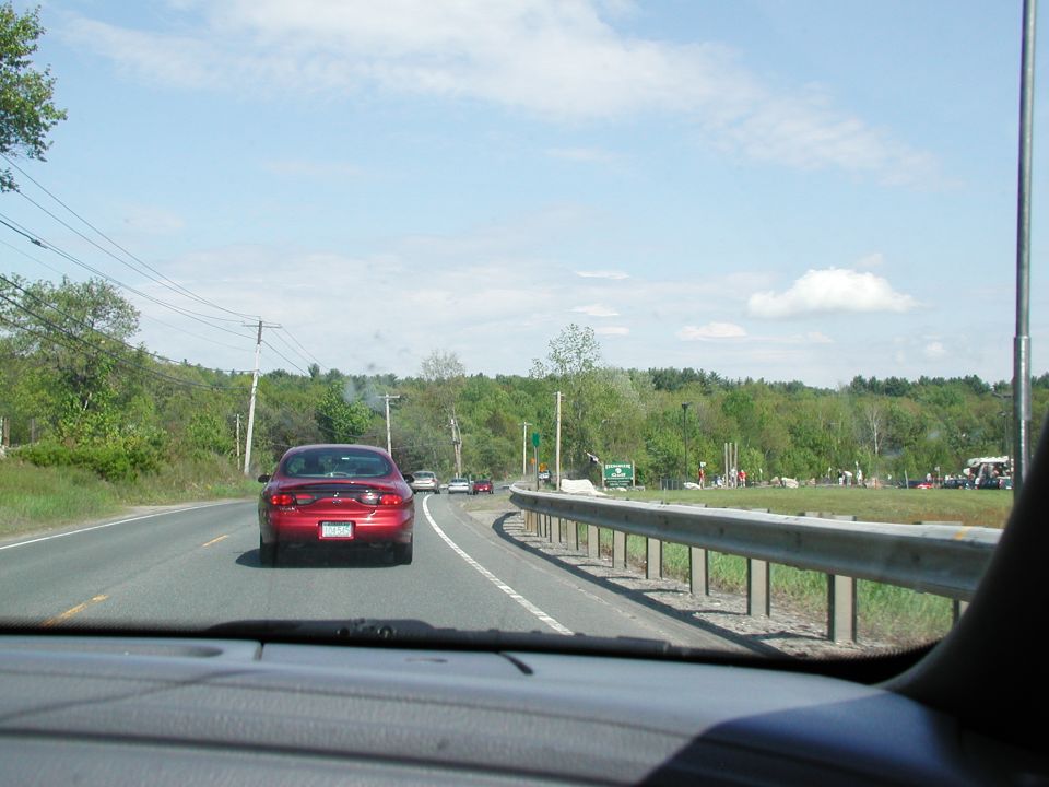 Red sedan driving on a highway, seen from behind