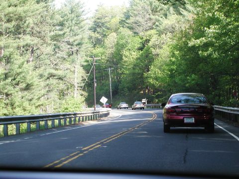 1992 Ford Taurus - A red sedan travels down a winding road surrounded by lush green trees.