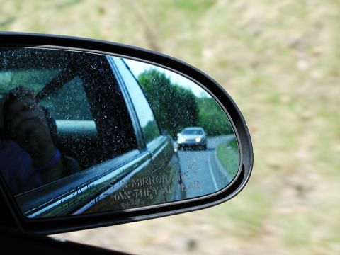 1992 Ford Taurus - Car seen in side mirror on a road with trees and grass alongside.