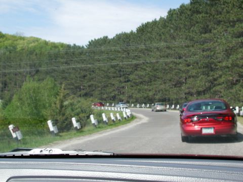 1992 Ford Taurus - A red 1992 Ford Taurus is seen from behind on a scenic, winding road with trees lining the route.