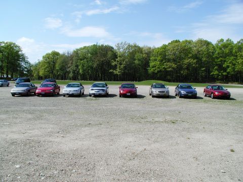 1992 Ford Taurus - A row of sedans are parked in a gravel lot under a partly cloudy sky.