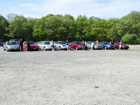1992 Ford Taurus - A group of people gathered around several sedans parked in an outdoor lot.