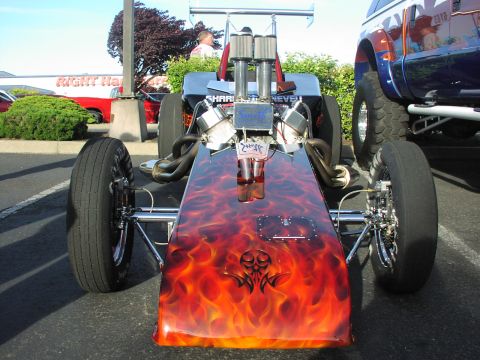 1979 Ford Bronco - A dragster with a flame paint job and tribal skull graphic is parked next to a lifted truck.