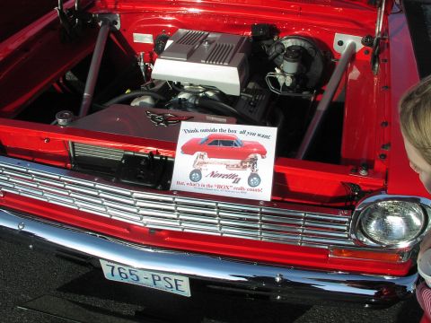 1979 Ford Bronco - Engine bay of a red car displays a sign with an illustration and text about "Noretta II".
