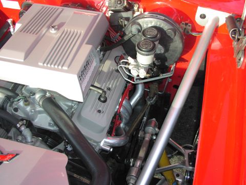 1979 Ford Bronco - The engine bay of a vehicle is shown with various components and a red exterior panel.