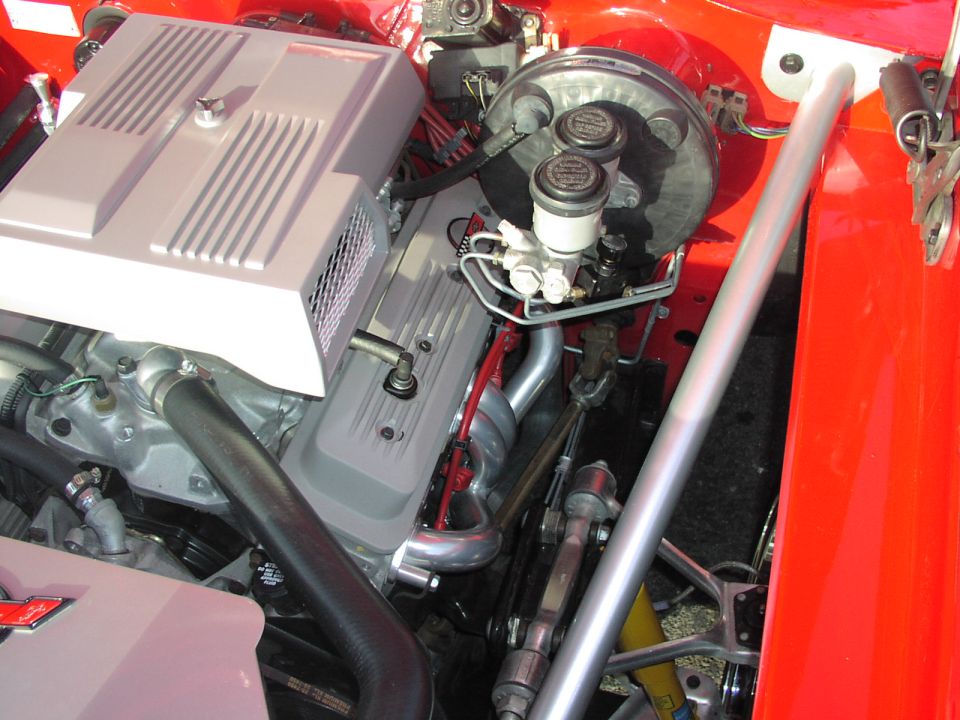 Close-up of a car's engine bay, showing the V8 engine, brake booster, and a silver strut tower bar