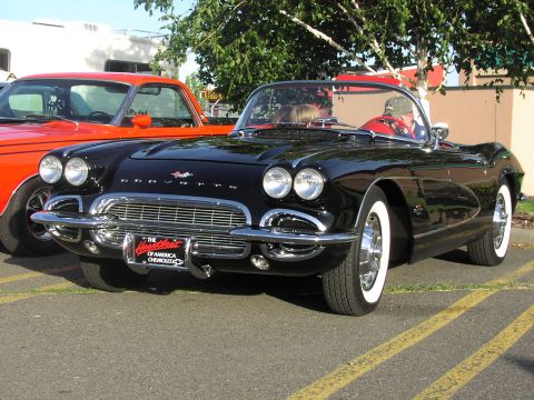 1979 Ford Bronco - A black 1959 Chevrolet Corvette convertible is parked next to an orange pickup truck.