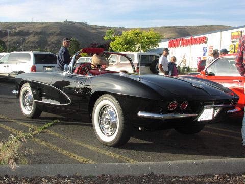 1979 Ford Bronco - A black 1958 Corvette convertible is parked in a lot with other vehicles and people around.