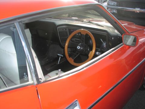 1979 Ford Bronco - Interior view of an orange vehicle, a wooden steering wheel and white upholstery.
