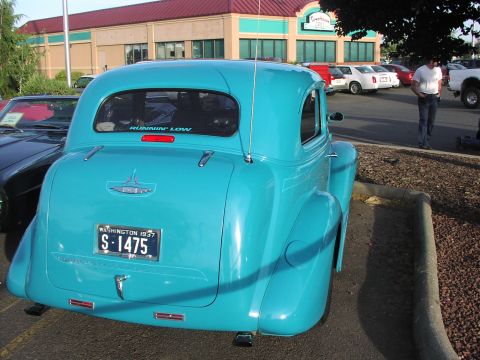 1979 Ford Bronco - A turquoise 1937 Chevrolet Coupe is parked in a lot, with other vehicles and a building in the background.