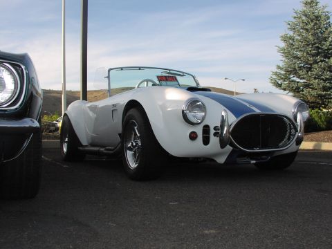 1979 Ford Bronco - A white AC Cobra replica with blue racing stripes is parked outside, with a 'For Sale' sign visible on the dashboard.