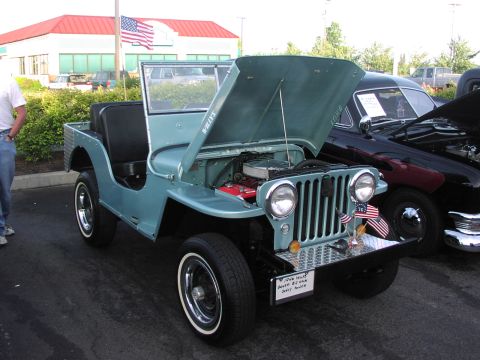 1979 Ford Bronco - A light blue Willys Jeep is parked with its hood open, displaying the engine. Another classic car is visible to the right.