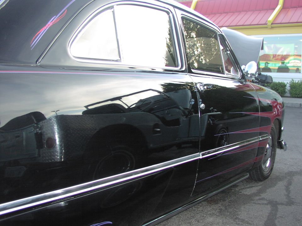 Black classic car with pinstripes on the side. Reflection shows a Jeep