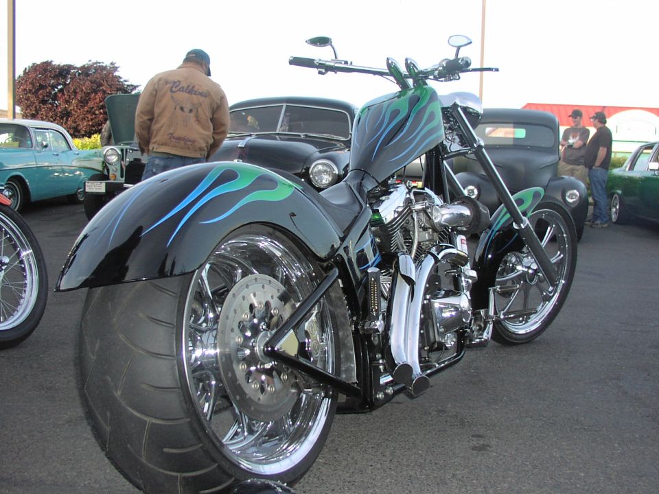 Chopper motorcycle with flame paint on the tank and fender, parked near classic cars