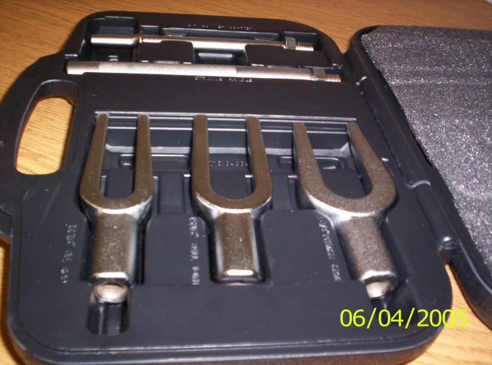 Black case with three forked ball joint separator tools and pins on a wood surface.