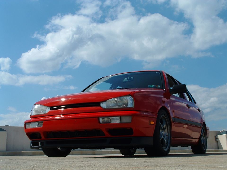Red Volkswagen Golf Mk3 parked under a cloudy sky