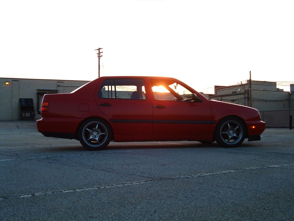 Red 1994 Volkswagen Jetta sedan, side view, sun glinting through the windshield