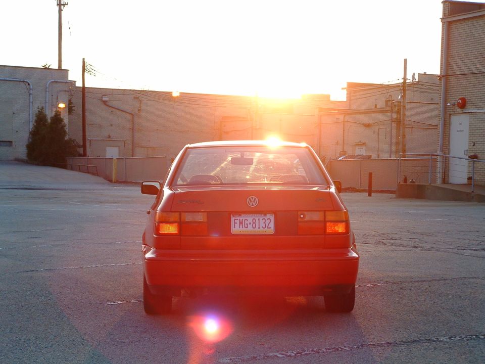 Red Volkswagen sedan parked in a lot at sunset, rear view